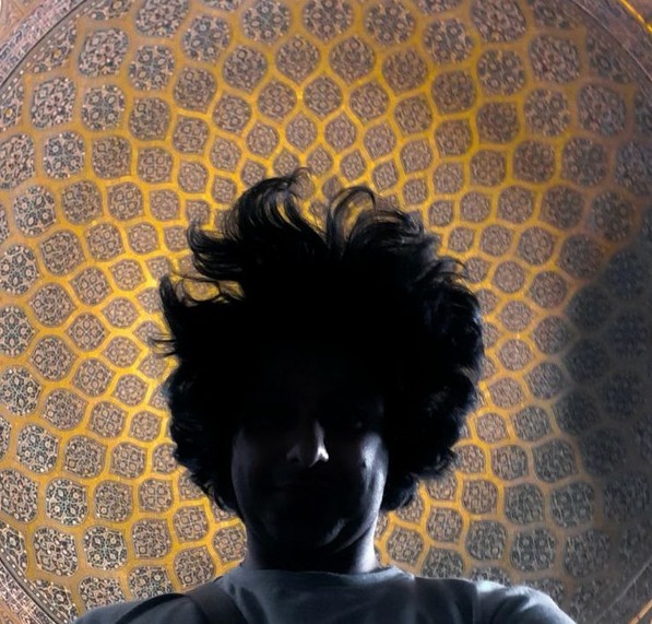 Hossein, backlit, looking down into the camera beneath a tiled, patterned dome